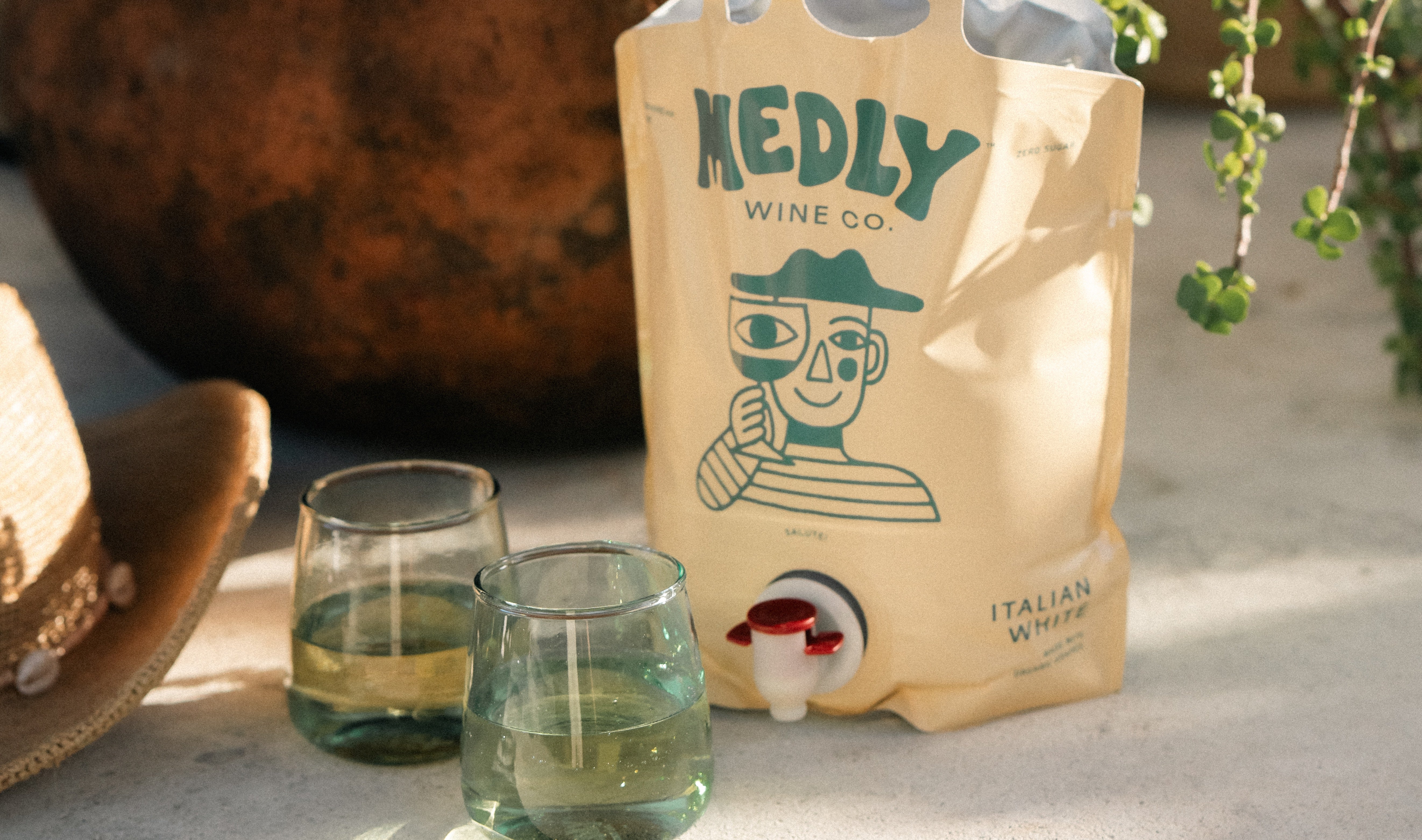 A pouch of Medly Italian white wine and two glasses sit in front of a ceramic planter.