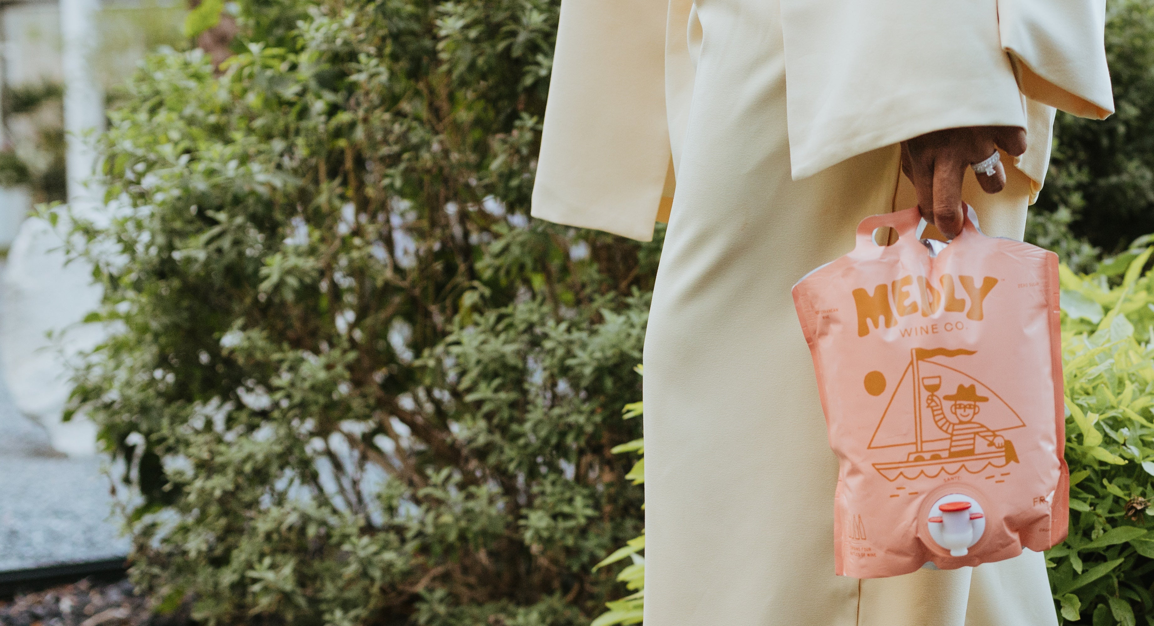 Person dressed for a special occasion holding a Medly Wine gluten free organic wine pouch outdoors.