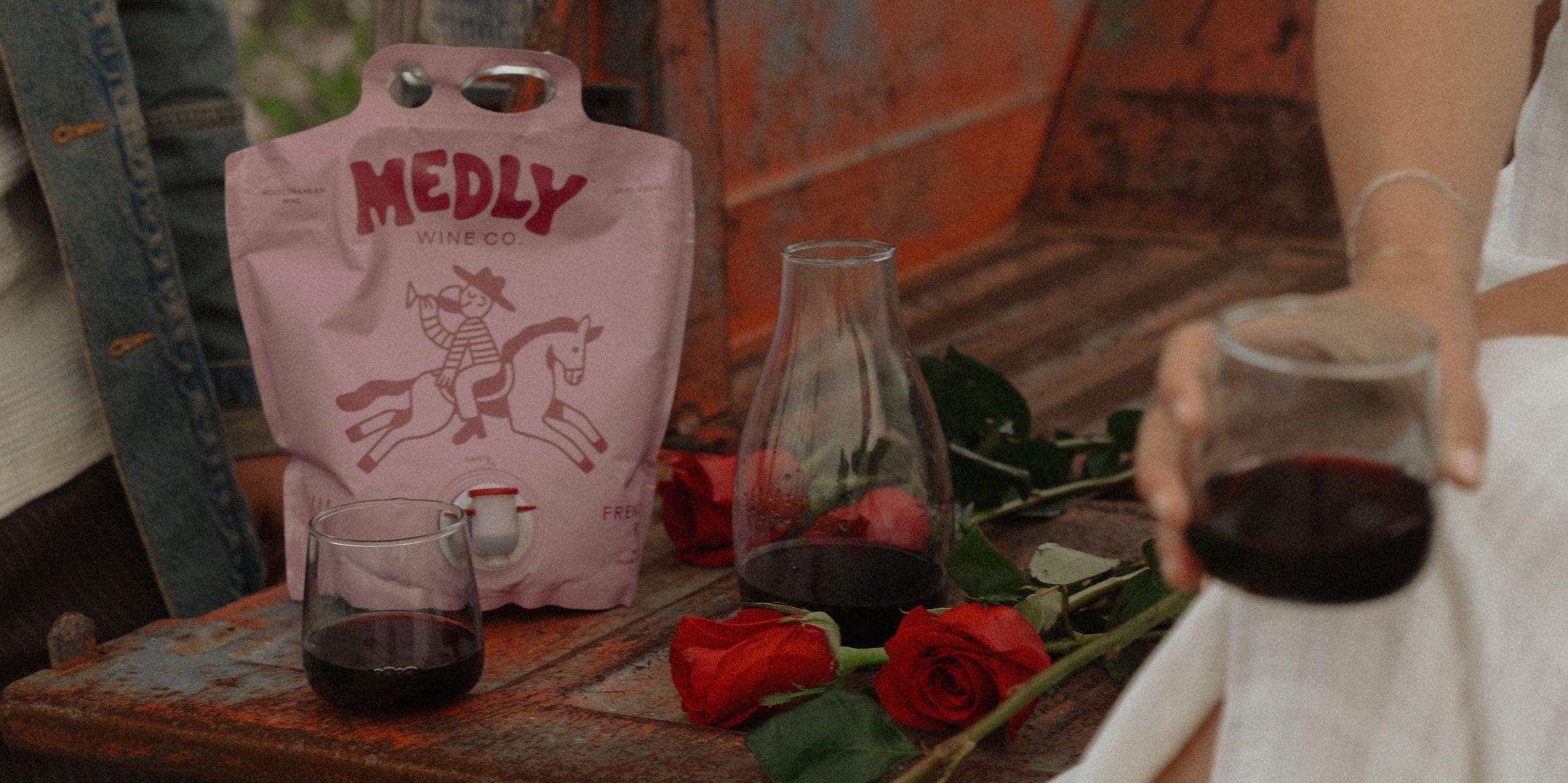 Valentine’s Day Wine, paired right: a couple pour and hold a Medly organic red wine pouch, nestled among roses on a vintage truck bed.