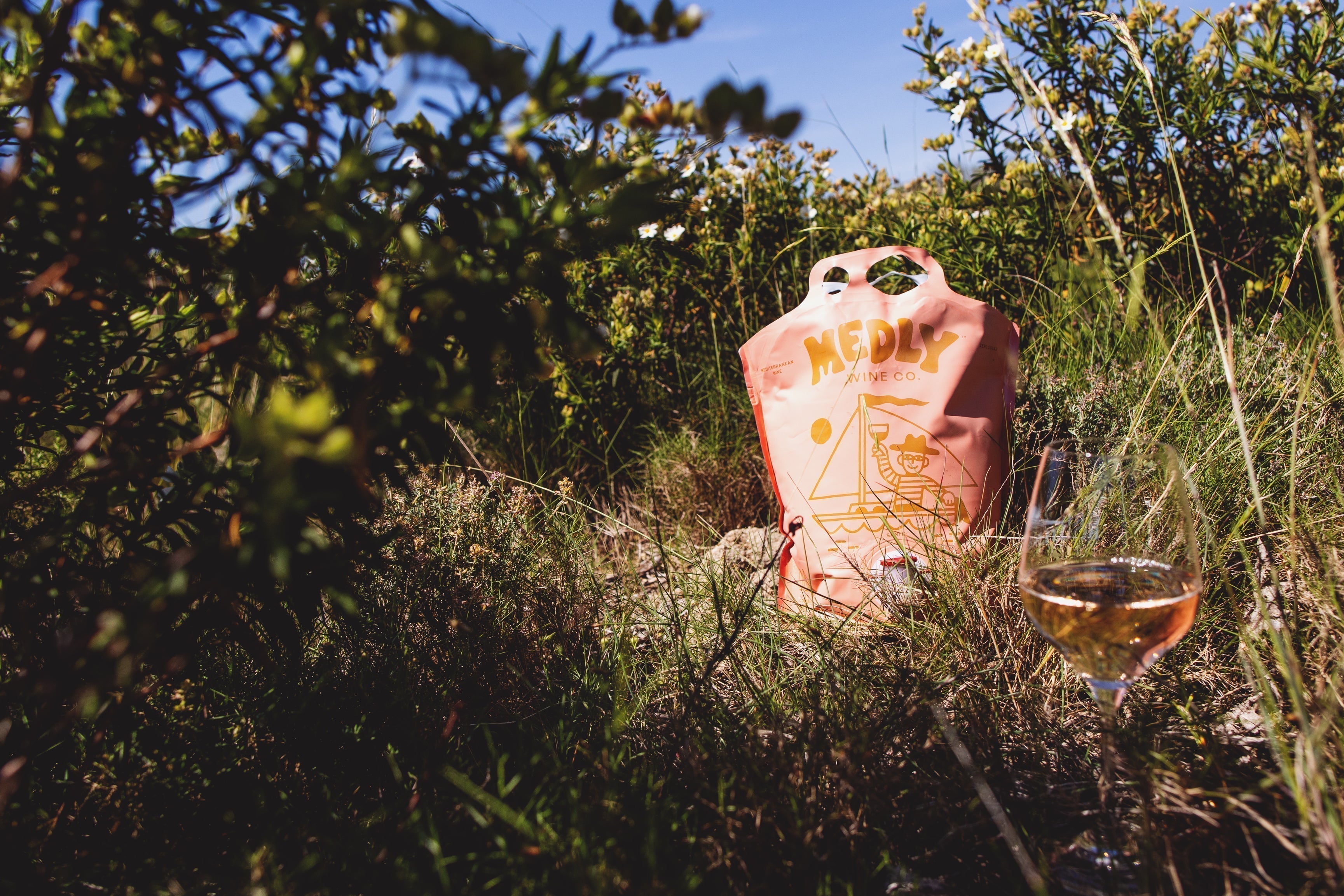  A Medly Wine pouch and glass of rose wine sit in a lush family-owned vineyard in the Mediterranean. 