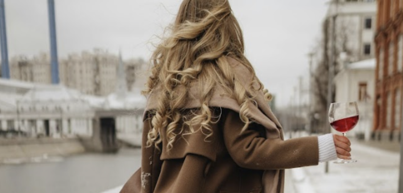 A blonde woman with a glass of Medly French Red wine in hand on a snowy winter walk.