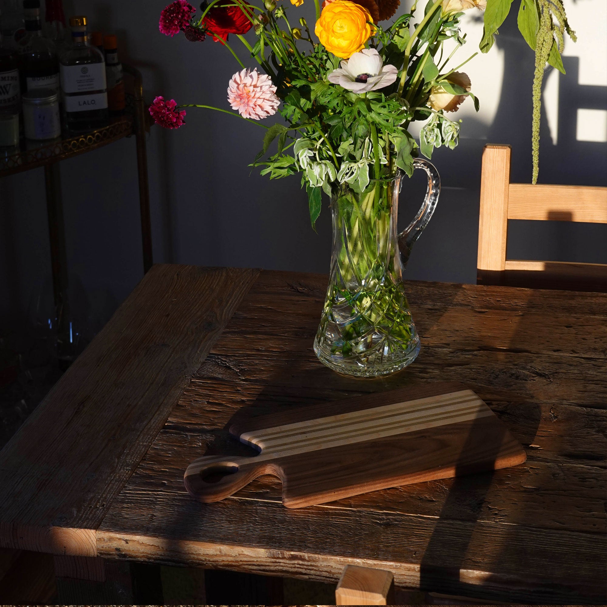 Clear glass pitcher filled with water and flowers on a wooden table.