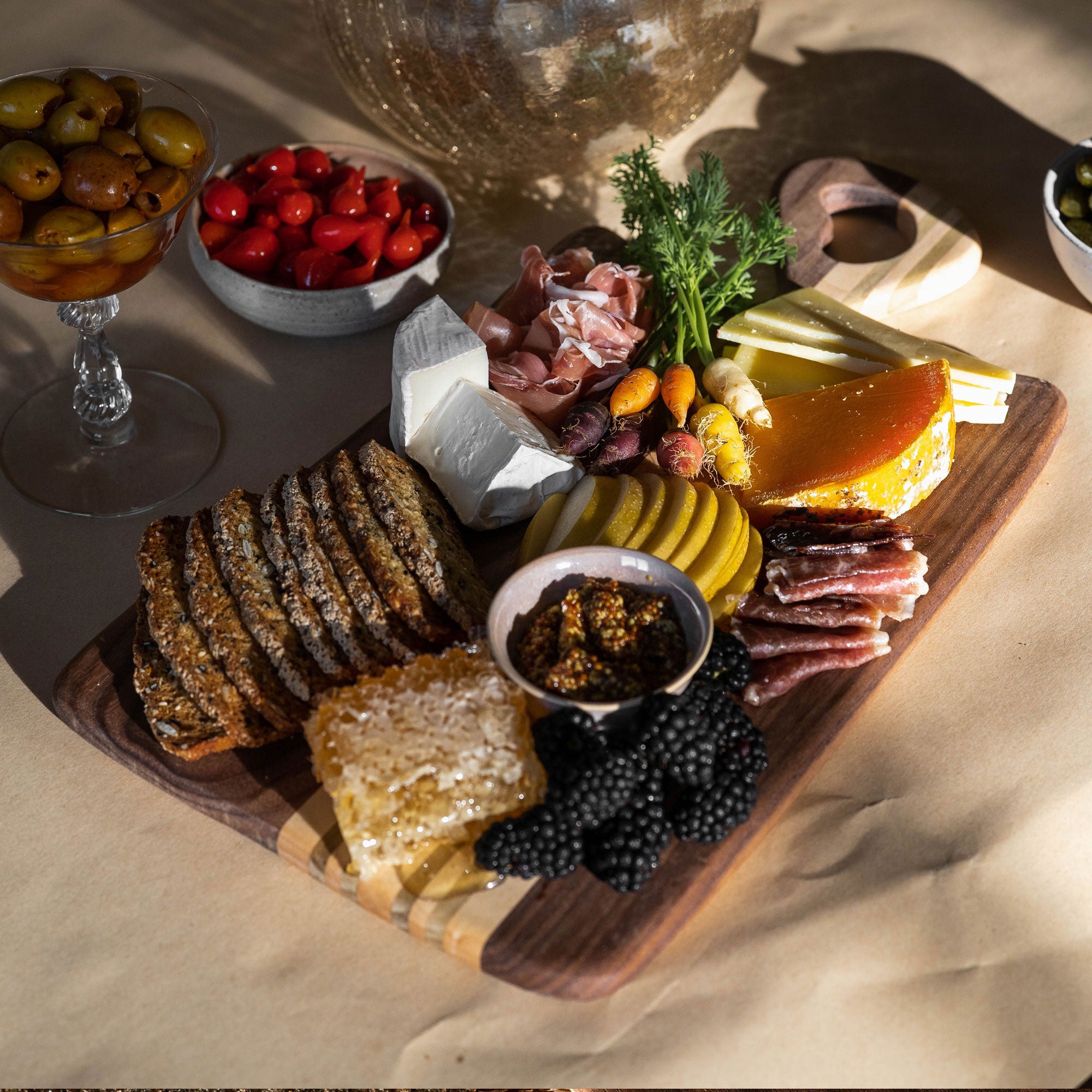 Hand Made wooden charcuterie board with various meats, cheeses, and fruits on a beige surface.